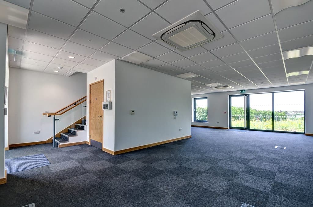 An open-plan commercial office floor with carpet tiles and a staircase