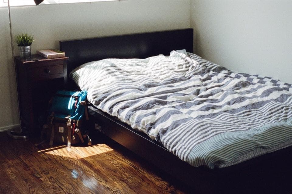 A family bedroom with a wooden bed frame, bedside table and backpack on the floor