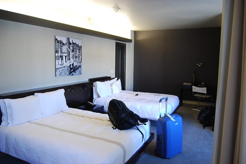 A twin hotel room with white bedding and a guest's suitcase and backpack