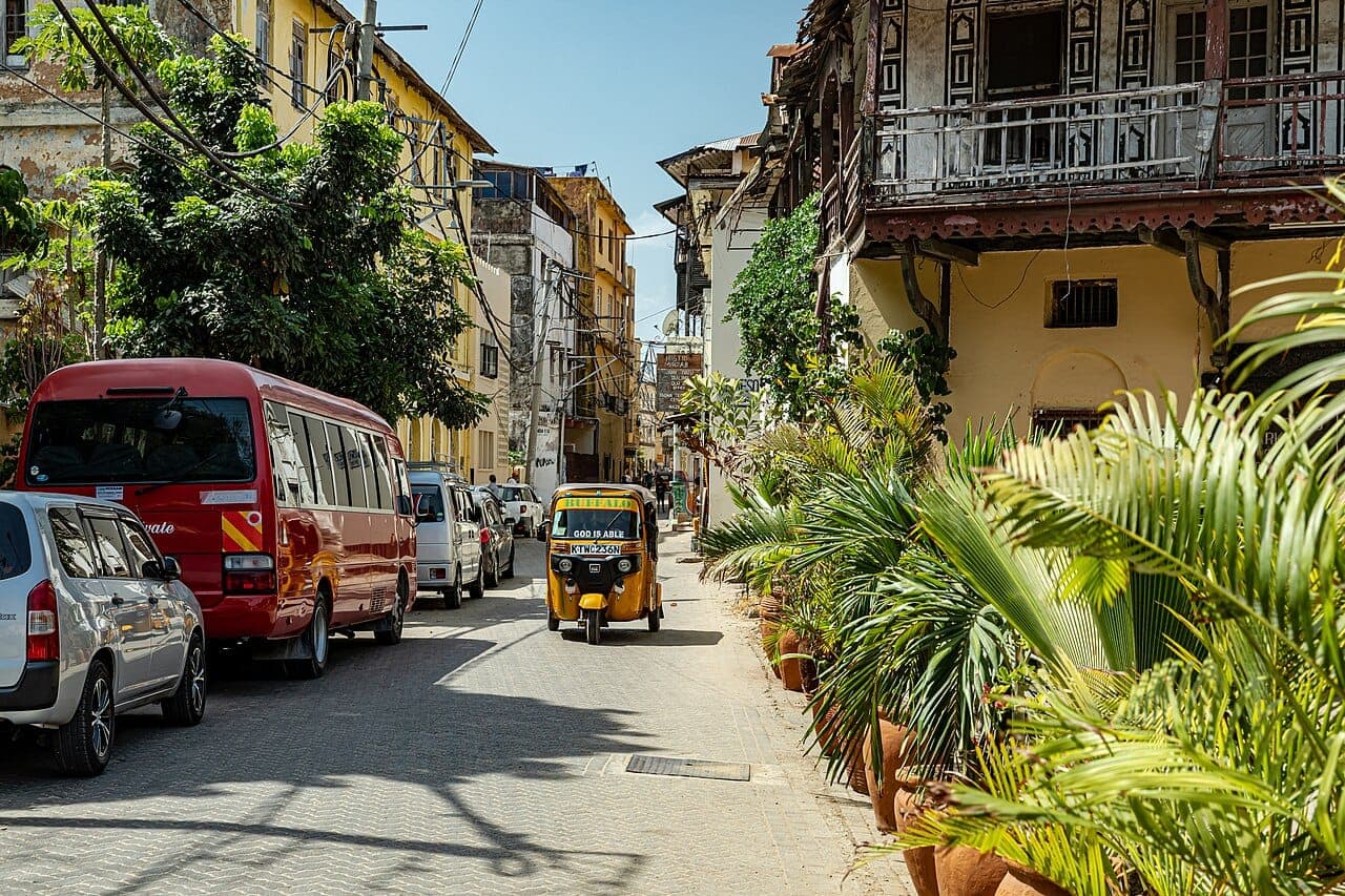 A street in Mombasa Old Town with balconied buildings, potted palms and a tuk-tuk